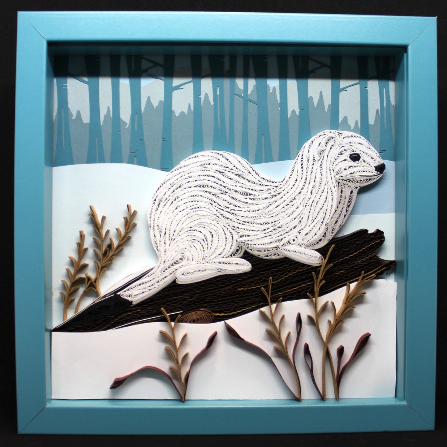 quillled paper artwork of white ermine on fallen log with dry weeds on the edge of a winter woodland